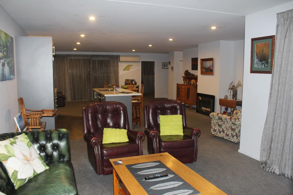 A living room with a green sofa, two leather armchairs, a wooden coffee table, and a dining area in the background.