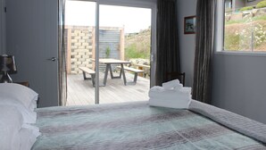 Ein Schlafzimmer mit Bett, Fenster und Blick auf eine Terrasse mit Tisch und Stühlen.