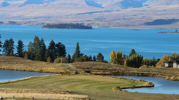 A golf course with a lake, mountains, and a small building in the distance.