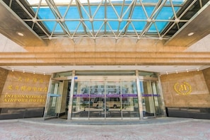 L'ingresso dell'Hotel vicino all'Aeroporto Internazionale, con facciata in vetro, un design geometrico del soffitto e un logo dell'hotel ben visibile.