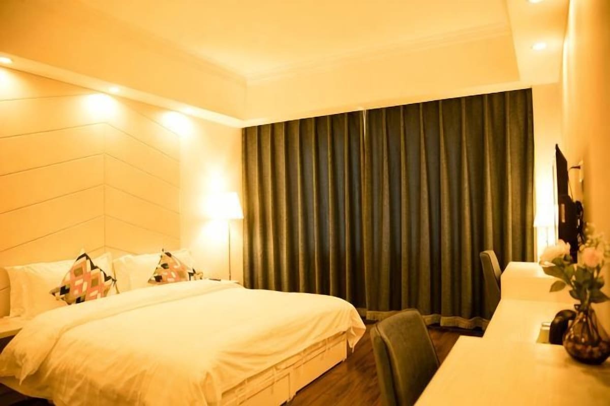 A hotel room with a bed, a desk, a chair, and a curtain.