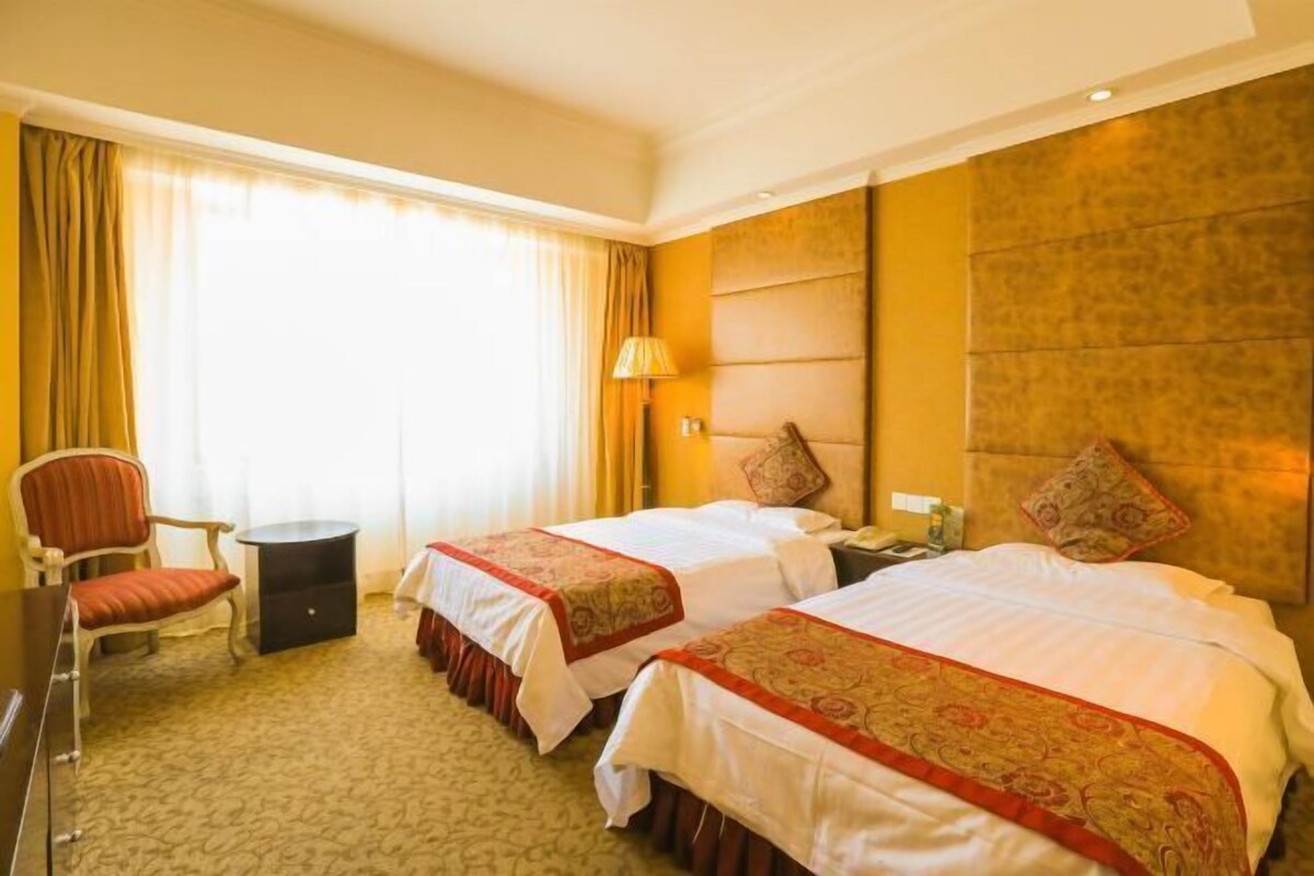 Habitación de hotel con dos camas, un escritorio, una silla y una ventana con cortinas.