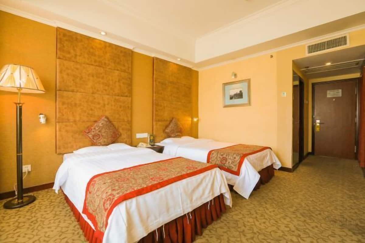 Ein Hotelzimmer mit zwei Betten, einer Lampe, einem gerahmten Bild und einer Tür.