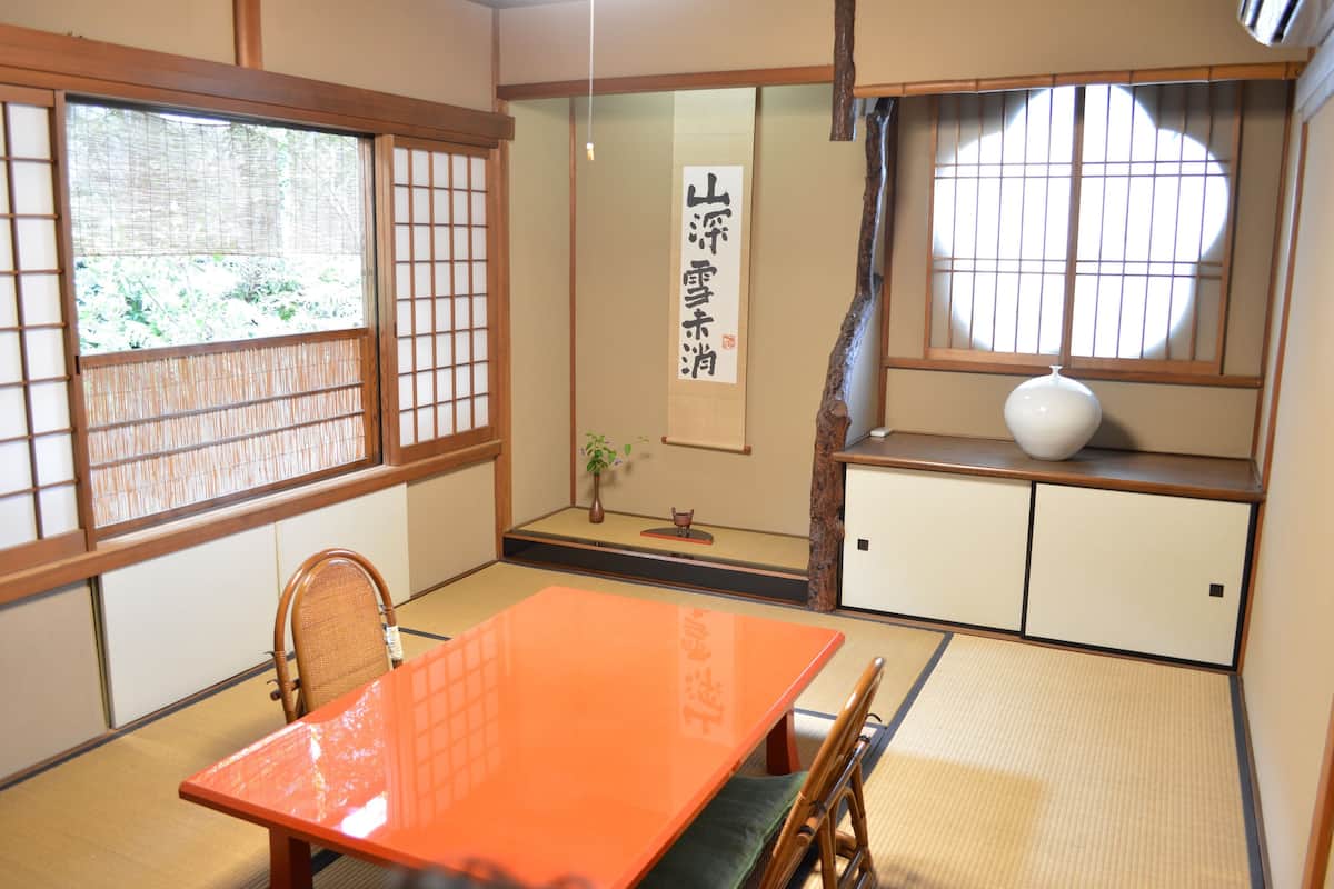 A traditional Japanese room with tatami flooring, a low orange table, and sliding doors with bamboo frames.