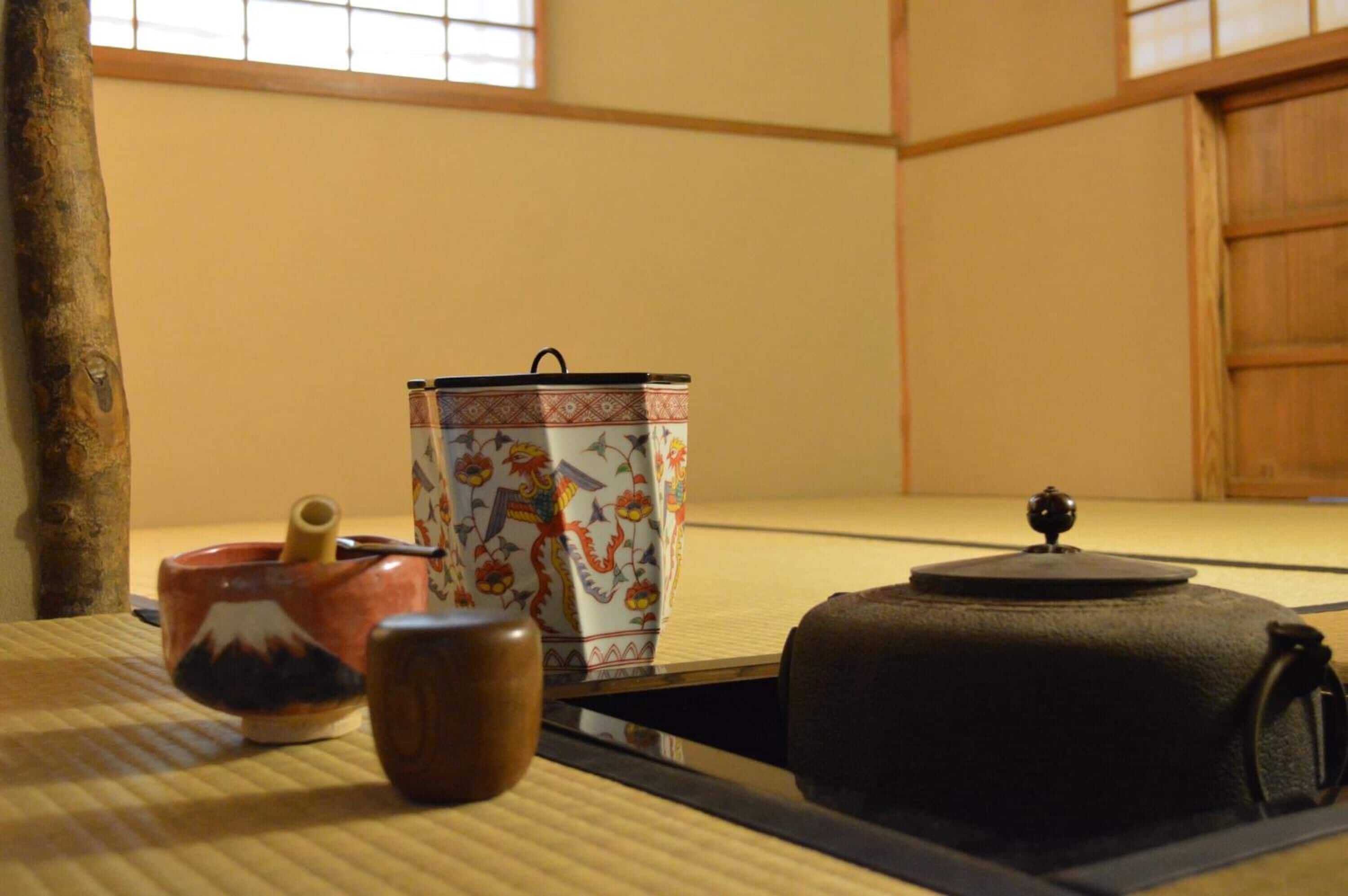 Et rum med tatamimåtter og et traditionelt japansk te-service, inklusive en keramisk kop, en te skål og en sort lakeret beholder.