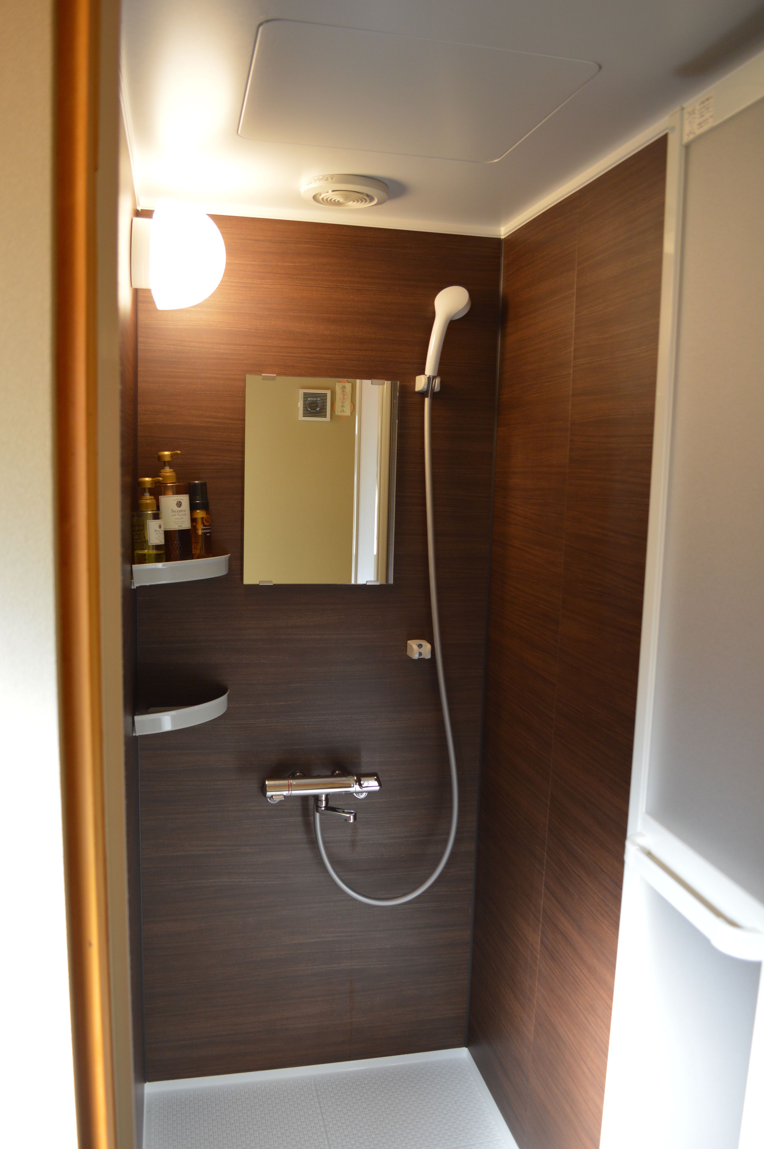 A small, modern shower with a handheld showerhead, a wall-mounted faucet, and a mirror above the sink.