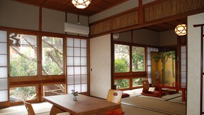 A traditional Japanese room with tatami flooring, wooden furniture, and large windows offering a view of trees. - Yadoya Manjiro (Kyoto)