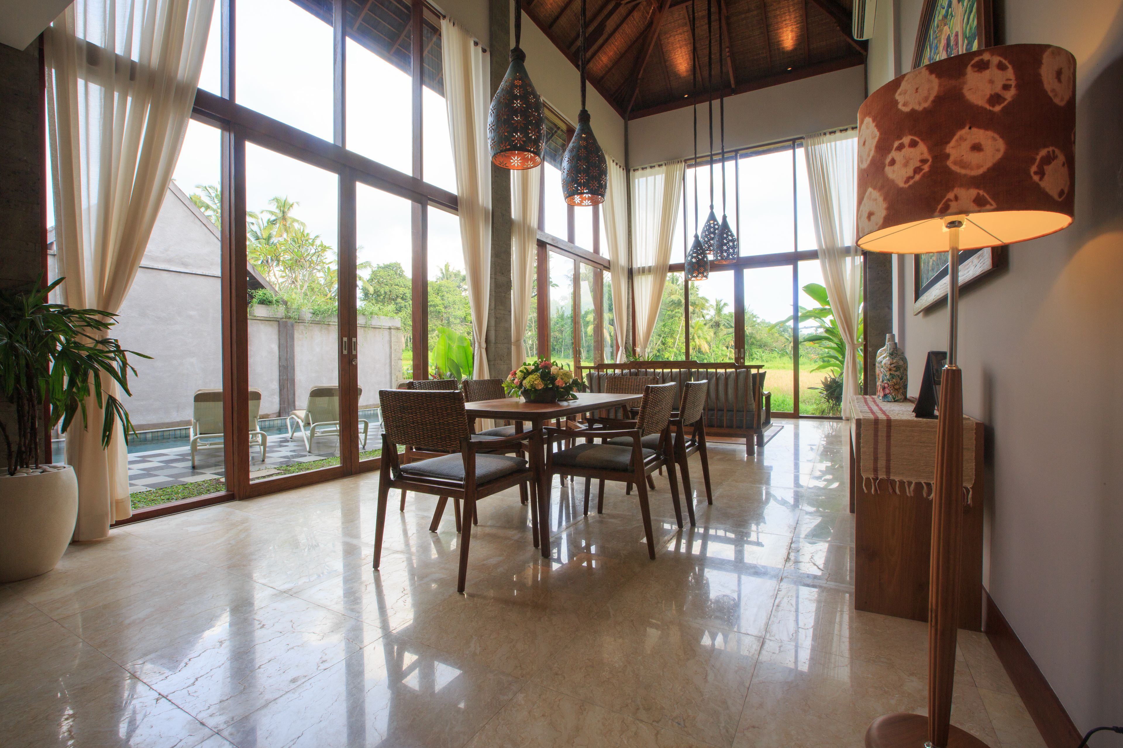 A spacious room with a large dining table and chairs, large windows with curtains, and hanging pendant lights.