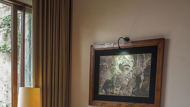A living room with a sofa, patterned cushions, a coffee table with books and a vase, a lamp, and a framed artwork on the wall. - Tejaprana Bisma (Ubud)