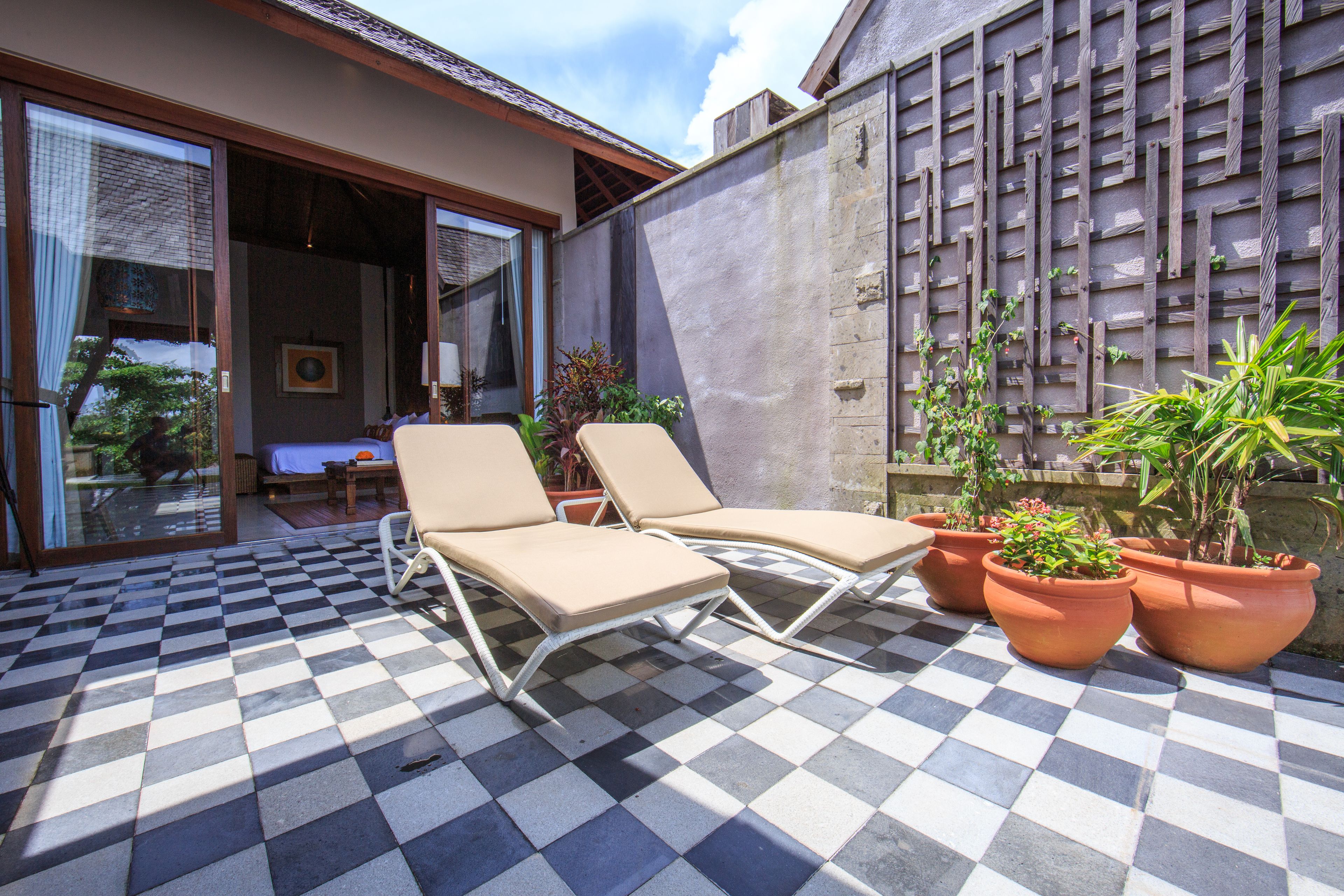 Un espacio al aire libre con diseño de cuadros, dos sillones de relax y plantas en macetas.