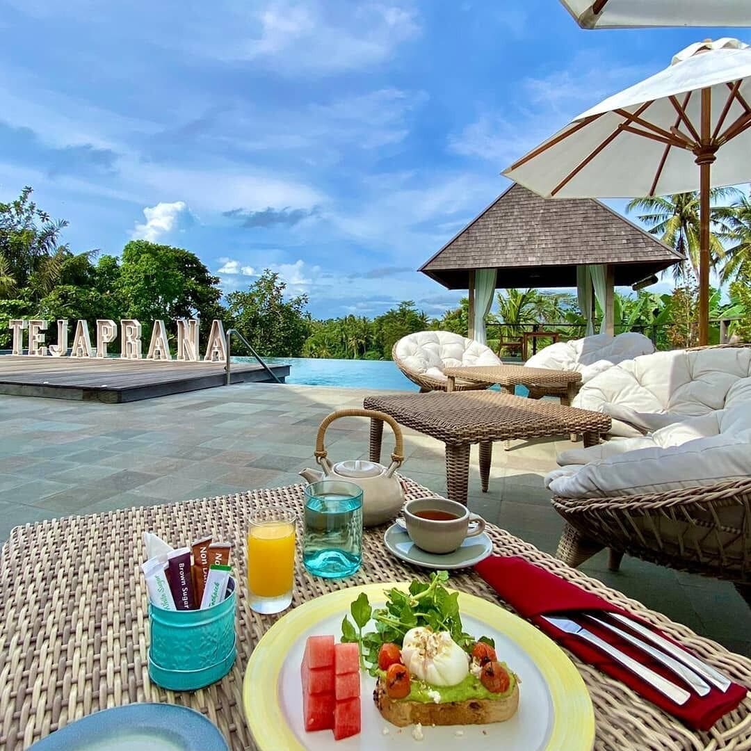 Un desayuno con un plato de comida, un hervidor de agua y una taza de café sobre una mesa con vista a una piscina y un pabellón.