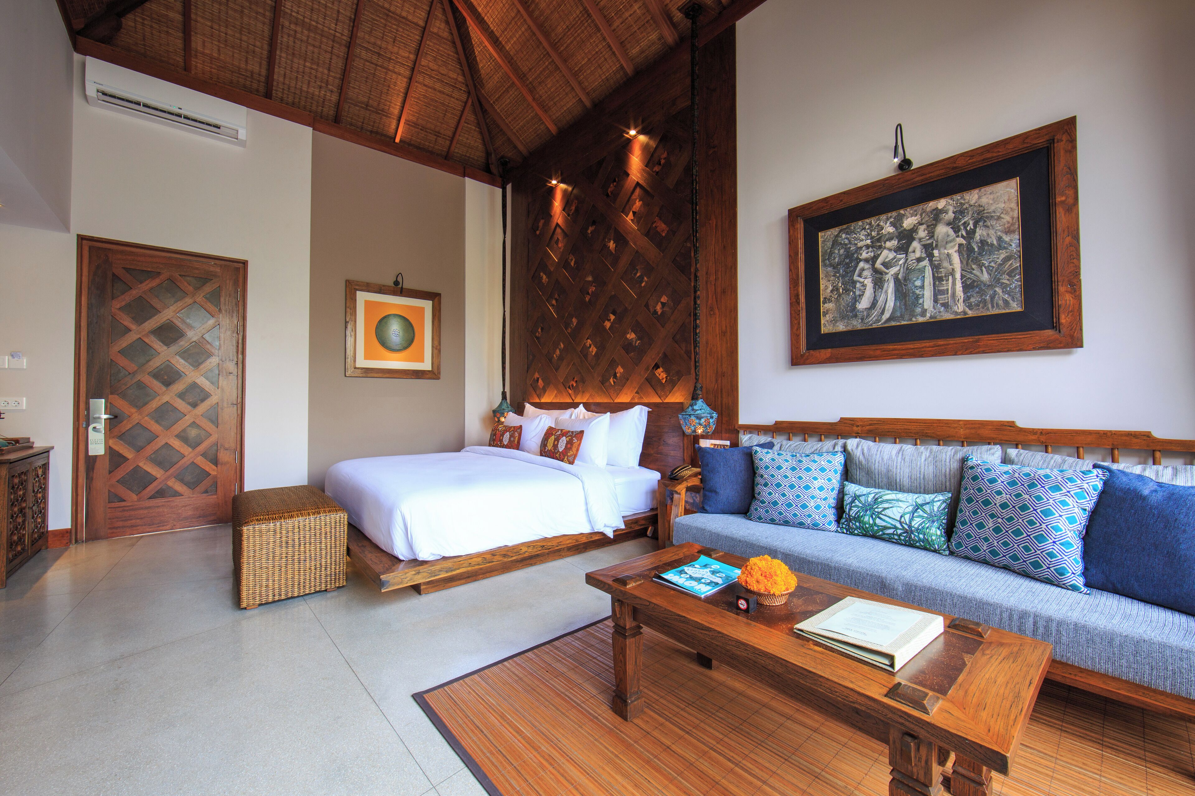 Een hotelkamer met een bed, een bank, een houten bijzettafeltje en een lijst met een afbeelding aan de muur.