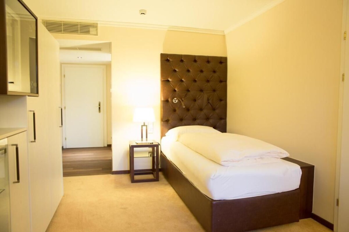 A hotel room with a bed, bedside table, and a mirror.