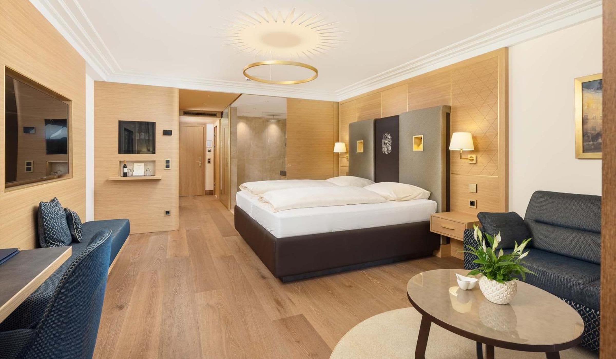 A modern hotel room with a large bed, a sofa, a small table, and a mirror.