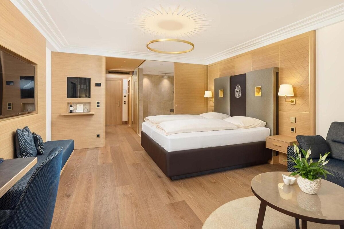 A modern hotel room with a large bed, a sofa, a small table, and a mirror.