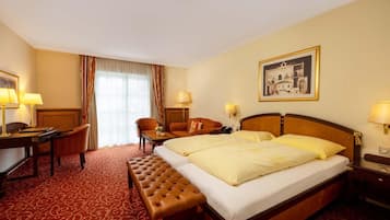 A hotel room with a bed, a desk, a chair, a bench, and a painting on the wall.
