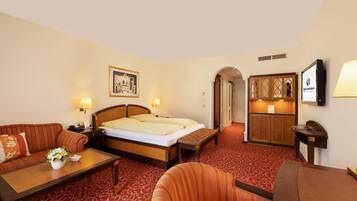 A hotel room with a bed, a sofa, a small table with a vase of flowers, a desk, and a cabinet.