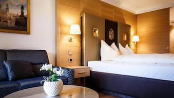 A hotel room with a bed, a sofa, a nightstand, a lamp, and a painting on the wall.