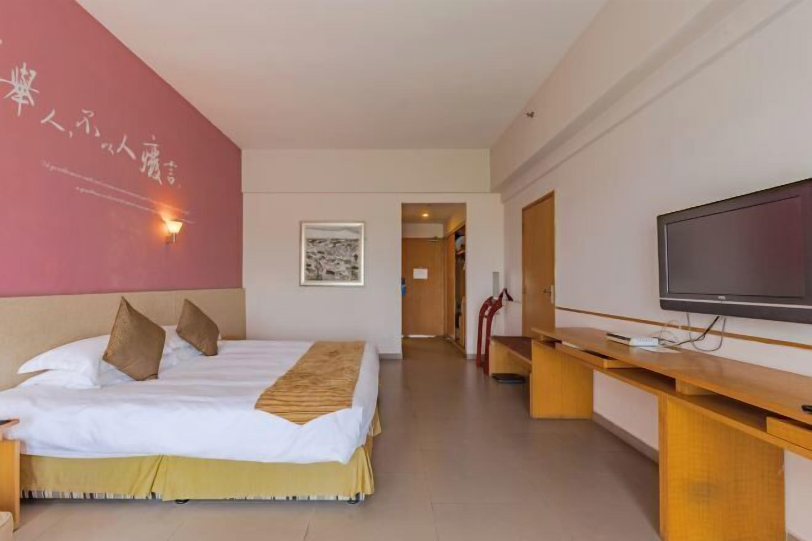 A hotel room with a bed, a television, a desk, and a red accent wall.