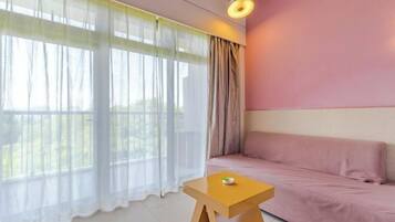 A room with a pink sofa, a wooden side table, sheer curtains, and a hanging light fixture.