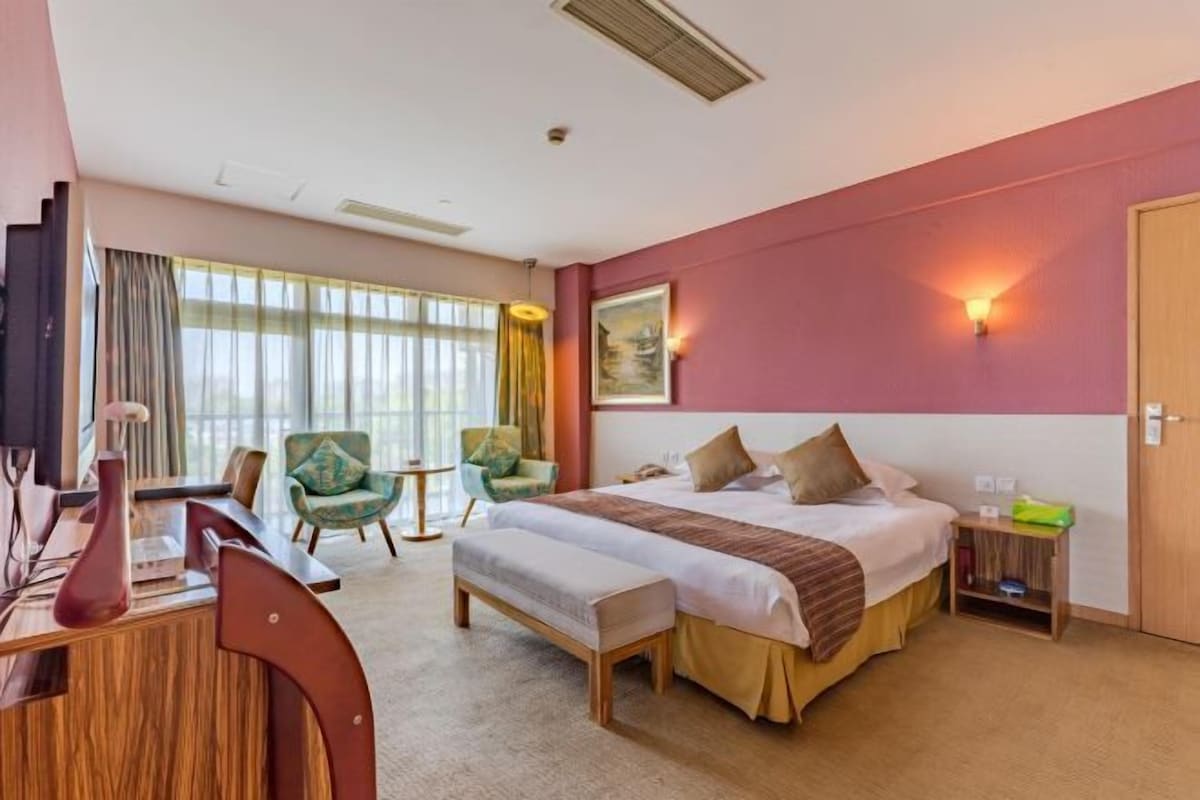 Une chambre d’hôtel avec un grand lit, un bureau avec une chaise, une petite table et une armoire.