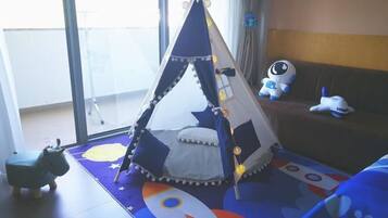 A child-friendly room with a teepee play area, a sofa with plush toys, and a colorful play mat.