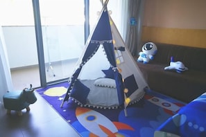 Une pièce conçue pour les enfants, avec un tipi servant d’espace de jeu, un canapé agrémenté de peluches et un tapis de jeu coloré.