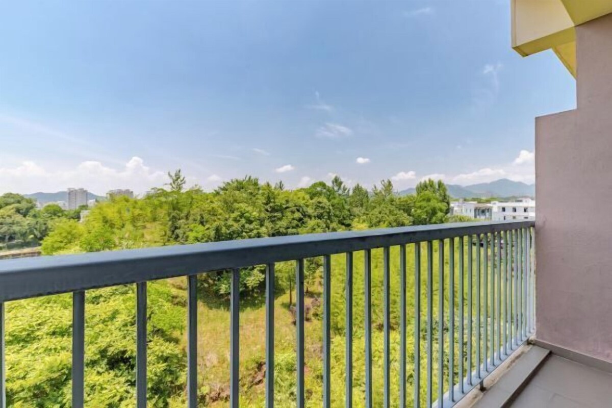 Un balcon doté d’une balustrade en métal, donnant sur un paysage verdoyant avec des arbres et des bâtiments situés au loin.