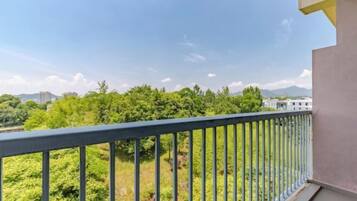 A balcony with a metal railing overlooking a green landscape with trees and distant buildings.