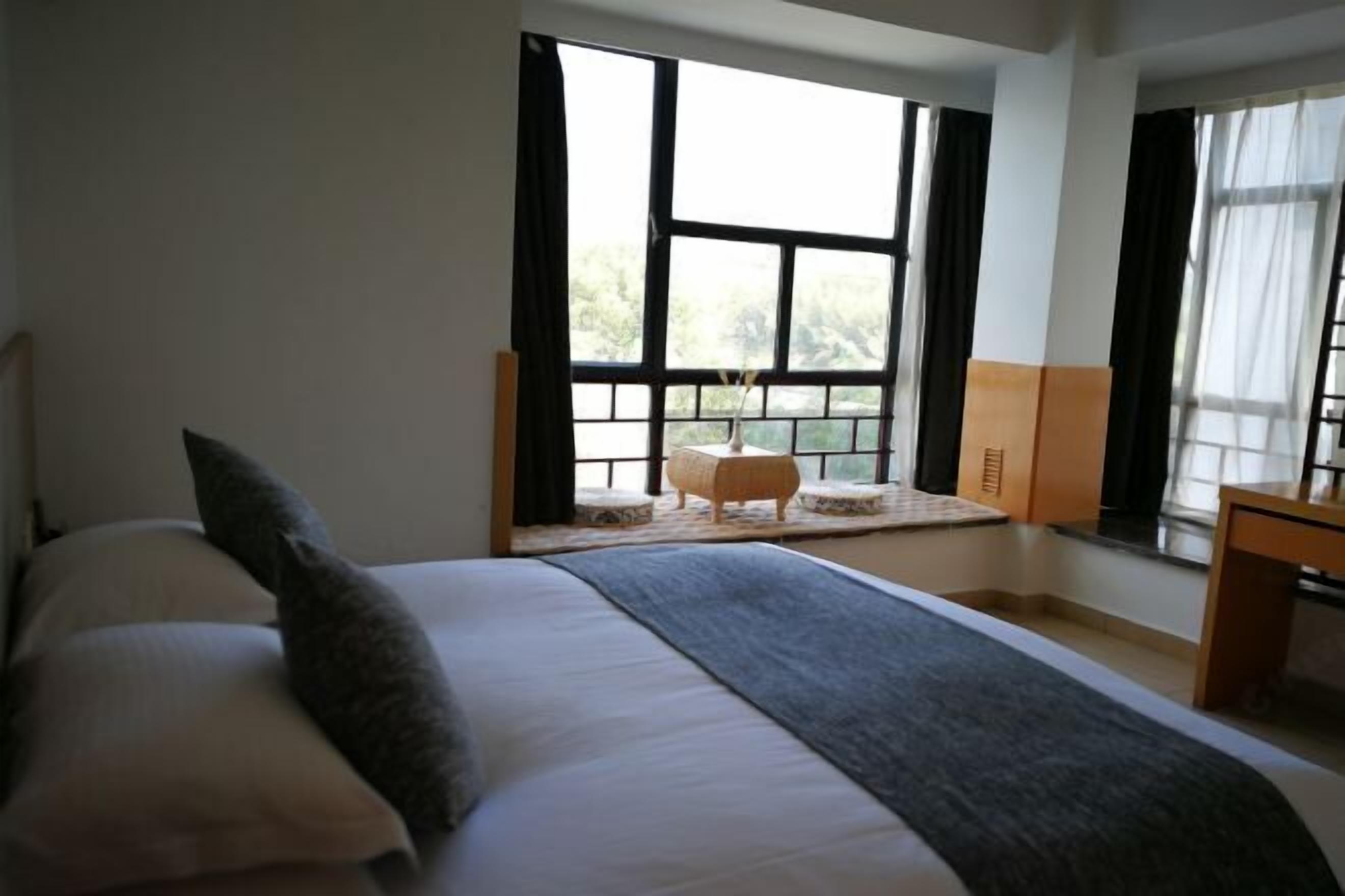 Une chambre avec un grand lit, une petite table et une fenêtre avec des rideaux.