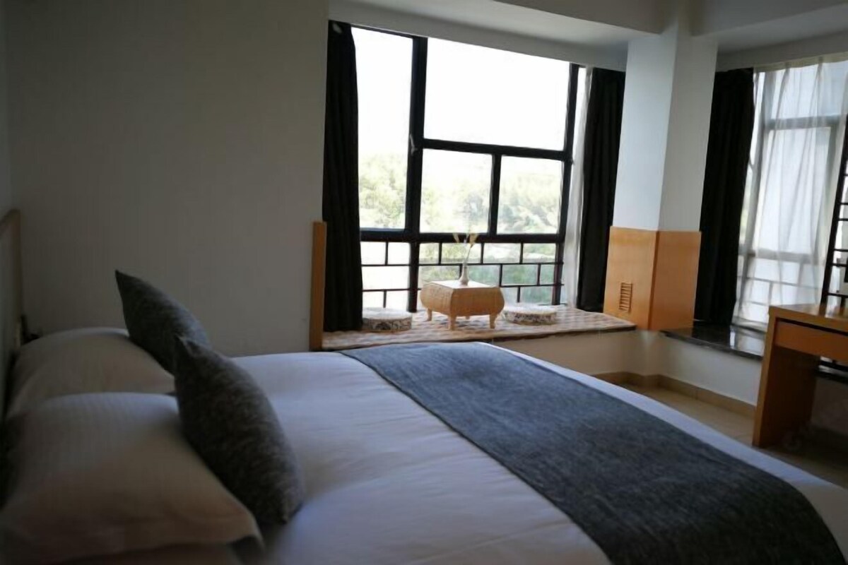 Une chambre avec un grand lit, une petite table et une fenêtre avec des rideaux.