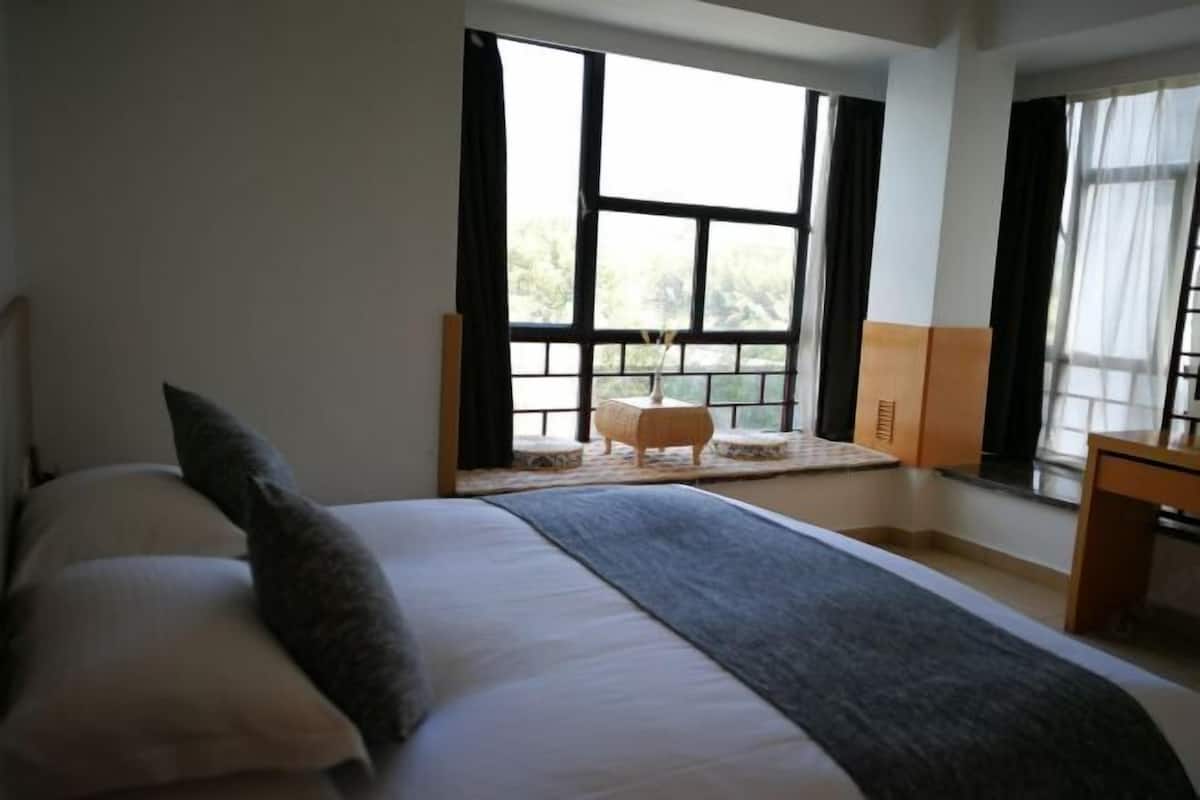 Un dormitorio con una cama grande, una mesita pequeña y una ventana con cortinas.