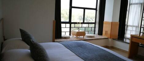 A bedroom with a large bed, a small table, and a window with curtains.
