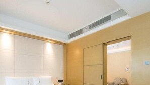 A modern hotel room with a large bed, a wooden floor, a sliding door leading to a seating area, and a visible air conditioning vent. - Shenzhen Pengker Deluxe Collection Hotel (Shenzhen)