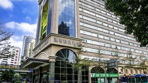 A multi-story hotel with a large glass facade, a prominent sign in a foreign language, and a green storefront below. - Shenzhen Pengker Deluxe Collection Hotel (Shenzhen)