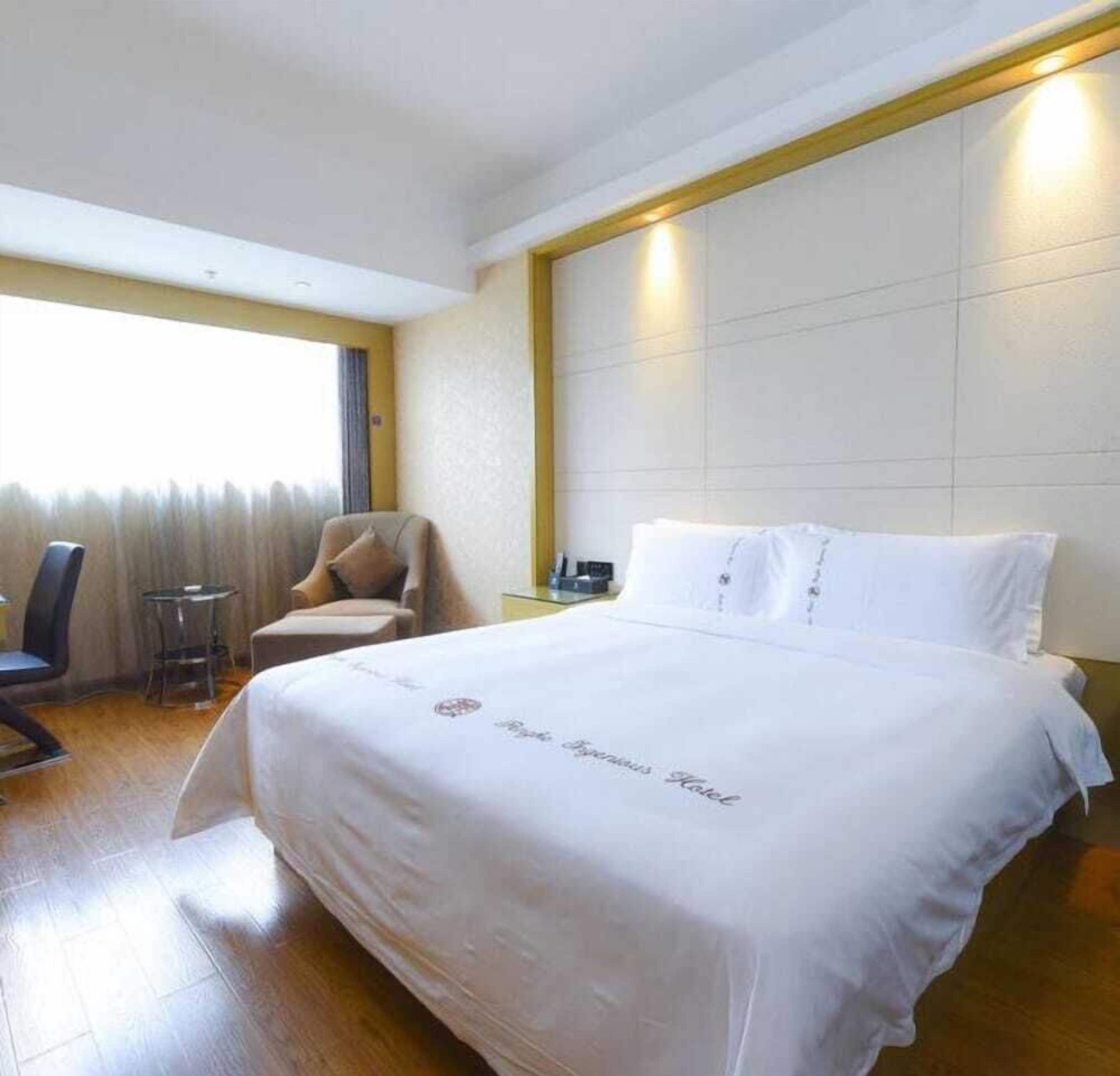 Een hotelkamer met een groot bed, een stoel, een tafeltje en een raam met gordijnen.