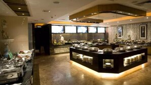 A buffet setup with multiple serving stations, a central island with covered dishes, and a kitchen area in the background. - Shenzhen Pengker Deluxe Collection Hotel (Shenzhen)