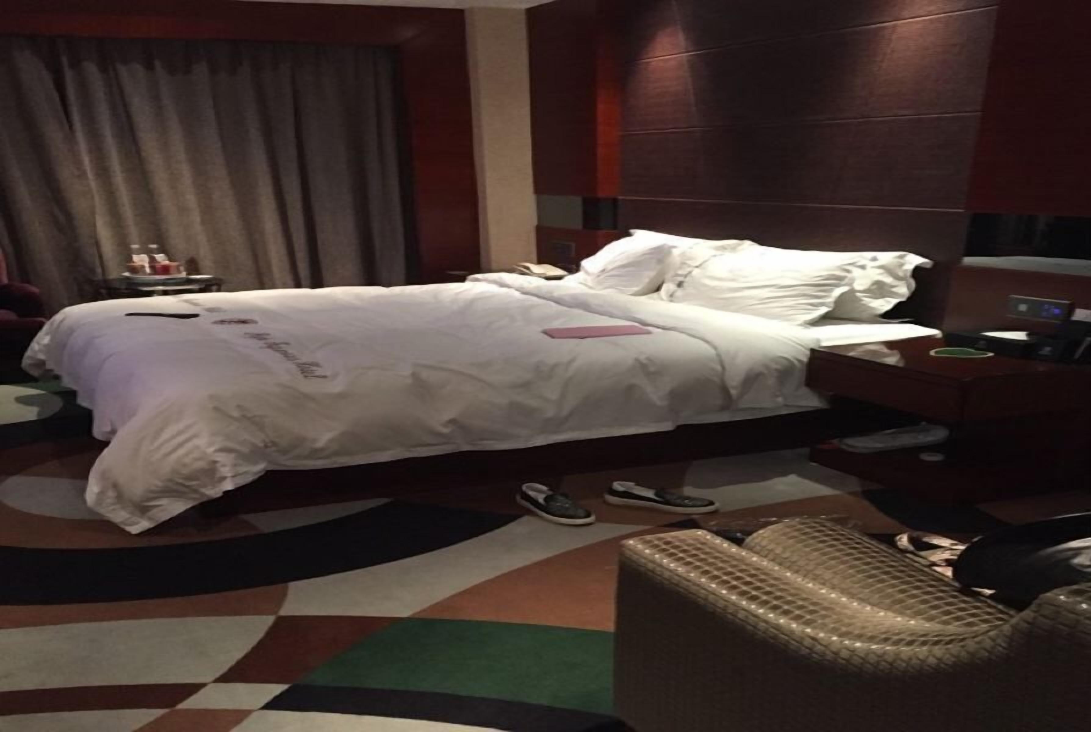 Una habitación de hotel con una cama grande, una mesita de noche, una silla y una pequeña mesa con lámpara.