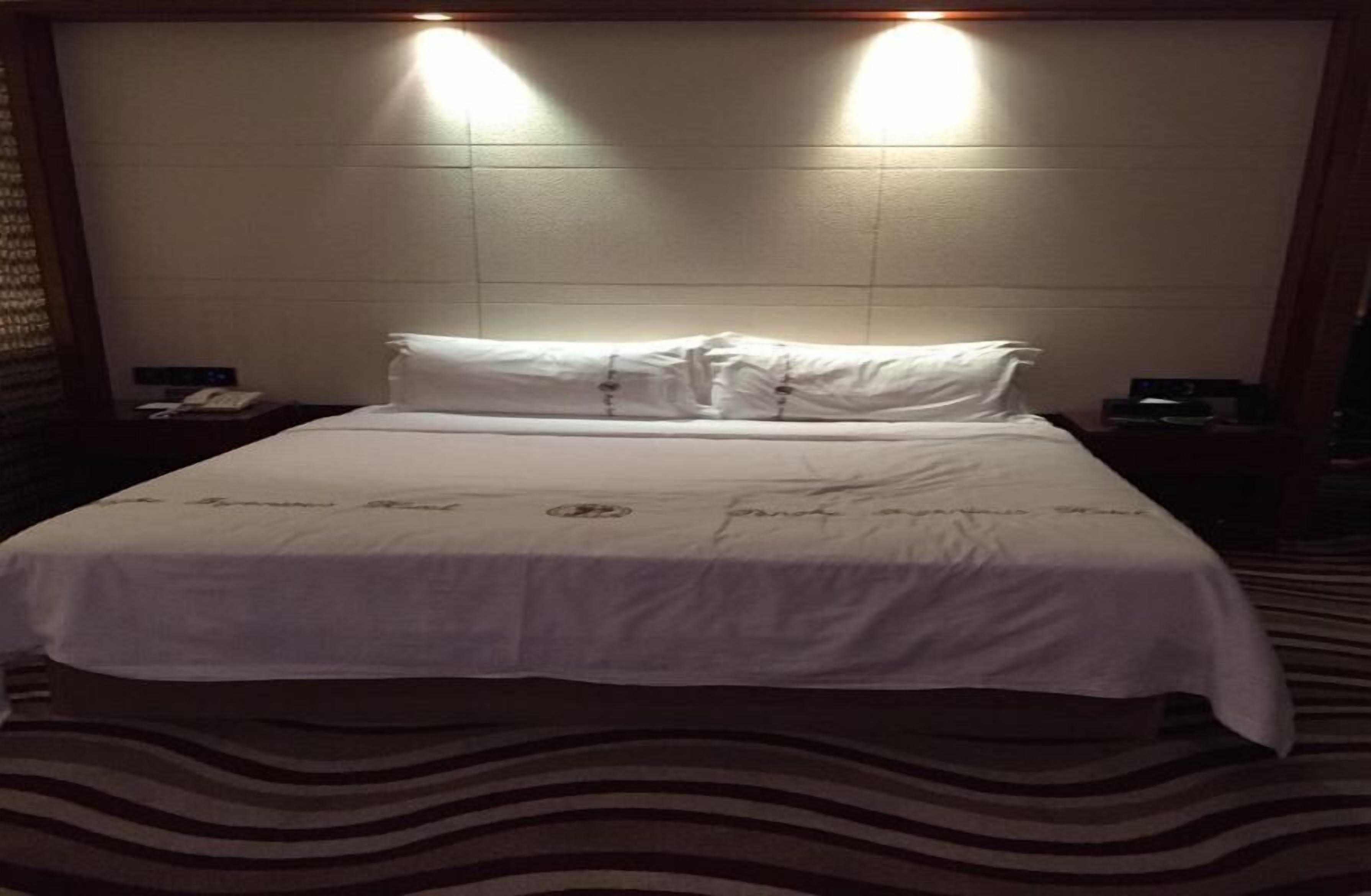 A hotel room with a large bed, two bedside tables, and a headboard with built-in lighting.