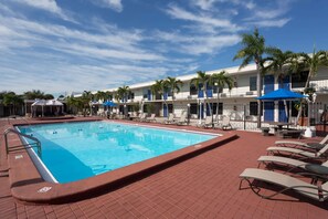 A swimming pool with lounge chairs and umbrellas, surrounded by a brick walkway and palm trees. - Super 8 by Wyndham St. Petersburg (St. Petersburg)