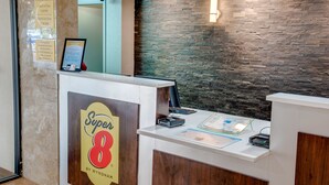 A reception desk with a stone wall backdrop, a sign for 'Super 8 by Wyndham', and a check-in/out time notice.