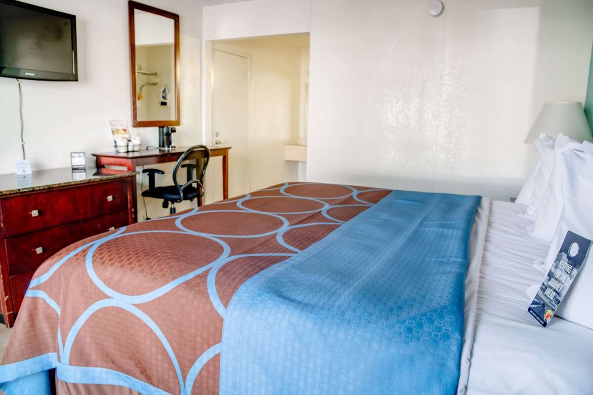 A hotel room with a bed, a desk, a chair, a television, and a bathroom visible through an open door.