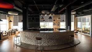 Un espace bar moderne doté d’un comptoir en pierre, de plusieurs luminaires suspendus et d’un coin salon avec des tabourets et des canapés.