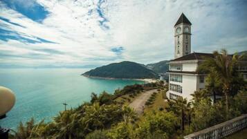 Vista costeira com uma torre do relógio, um edifício branco com grandes janelas e céu claro.