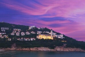 Une ville côtière avec des bâtiments construits sur une colline, un imposant bâtiment blanc doté d’une tour, et une mer calme.