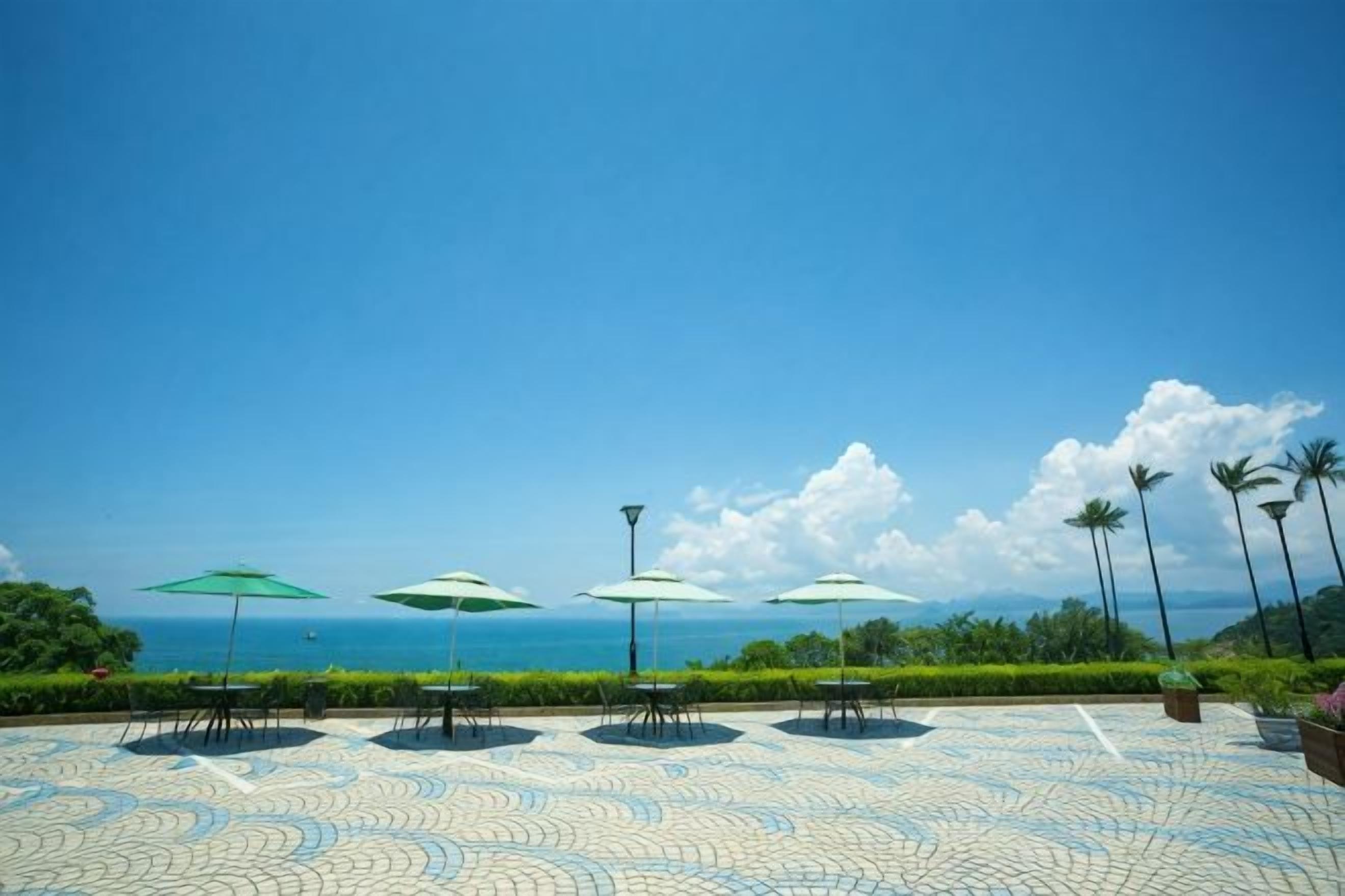 Uma área externa com ladrilhos, guarda-sóis e vista para o mar.