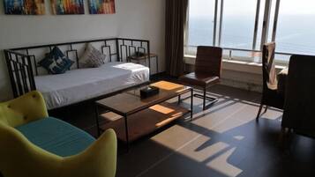 A room with a bed, a small table, two chairs, and a large window with a view of the sea.