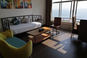 Ein Zimmer mit einem Bett, einem kleinen Tisch, zwei Stühlen und einem großen Fenster mit Meerblick.