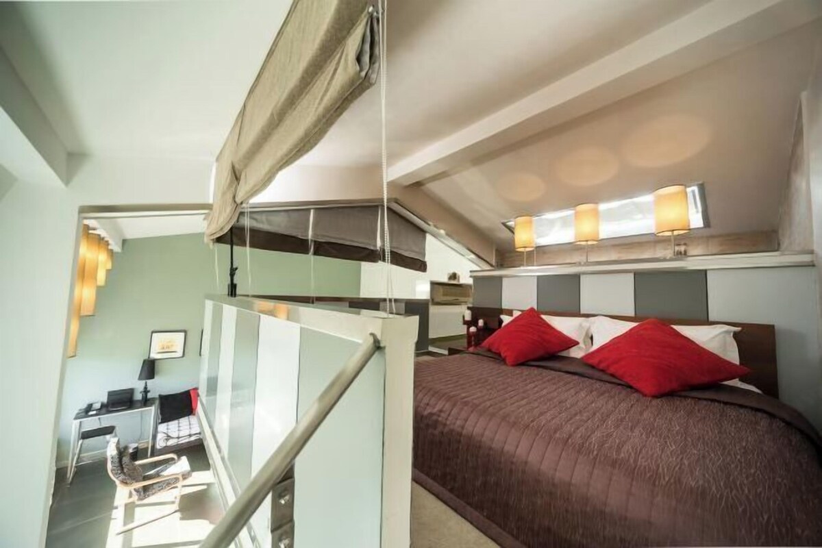 Ein Schlafzimmer mit einem Bett, roten Kissen, einem Schreibtisch mit Stuhl und einer Treppe.