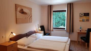 Een hotelkamer met een bed, nachtkastje, lamp, bureau, stoel en een raam met gordijnen.